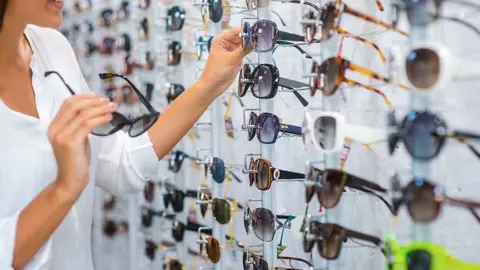 Choosing sunglasses in store. Close-up of cheerful young woman choosing sunglasses in store